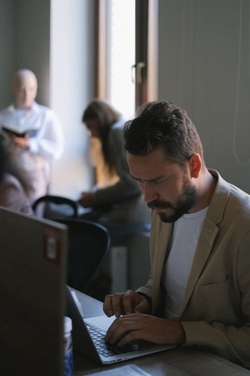 Focused man browsing laptop in office with people