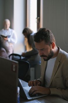 Serious male typing on netbook while working in conference room with colleagues on blurred background in office