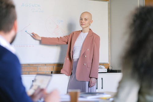Free Content female looking at camera and pointing with marker at whiteboard with diagrams while explaining marketing plan to colleagues in conference room during briefing Stock Photo