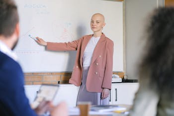 Content female looking at camera and pointing with marker at whiteboard with diagrams while explaining marketing plan to colleagues in conference room during briefing