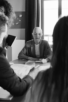 Black and white of focused female with unrecognizable colleagues gathering at table with documents during brainstorm in modern conference room