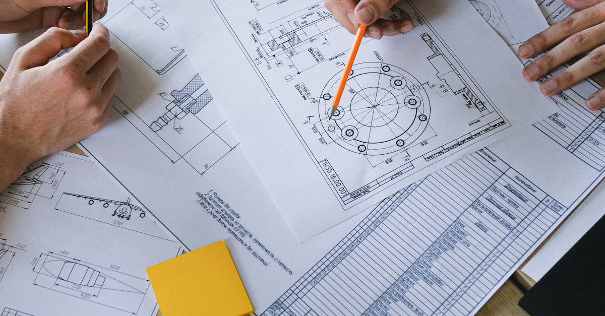 Group of colleagues discussing engineering plan on papers at table ...