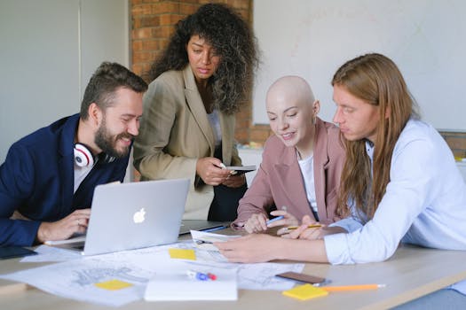 A diverse group of professionals engaged in a collaborative meeting around a laptop and papers.