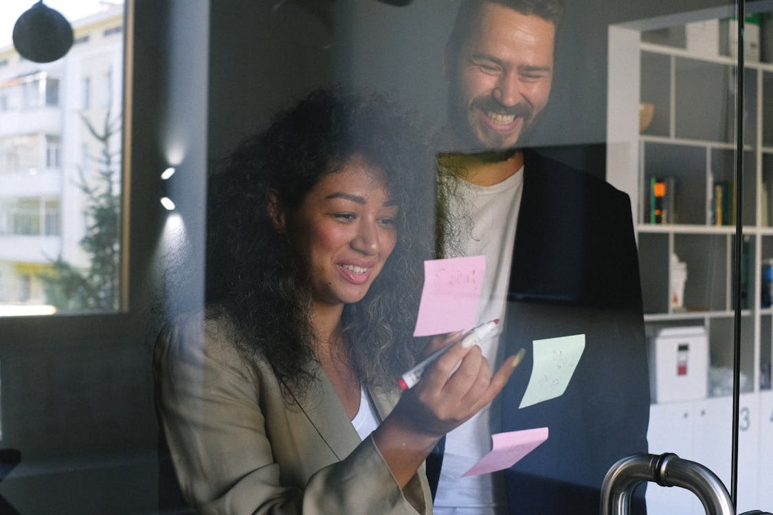 Free Diverse happy business partners checking stickers on glass door and smiling together in office Stock Photo