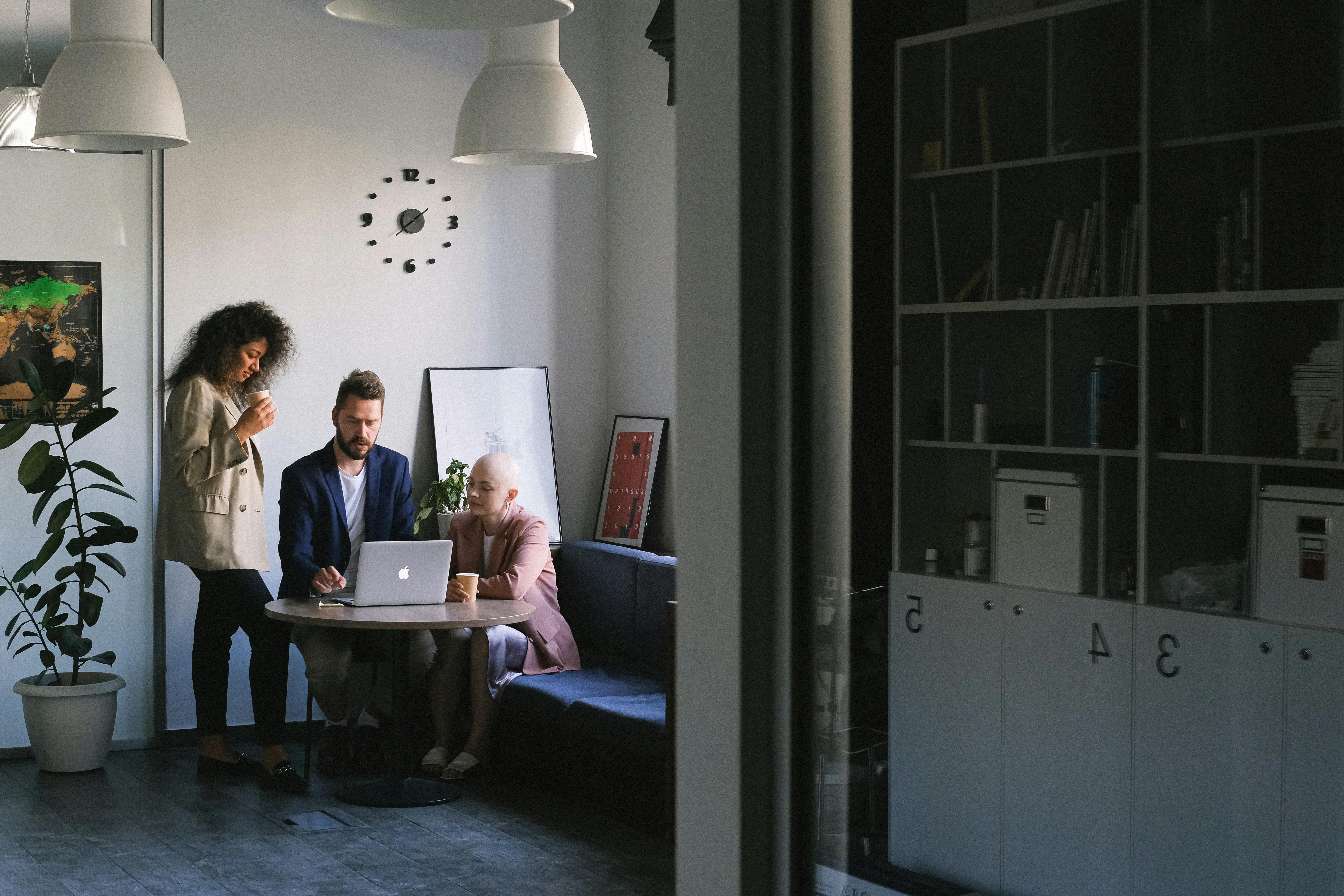 diverse colleagues talking about job while using laptop in office