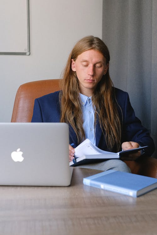 Serious entrepreneur reading notebook while browsing laptop