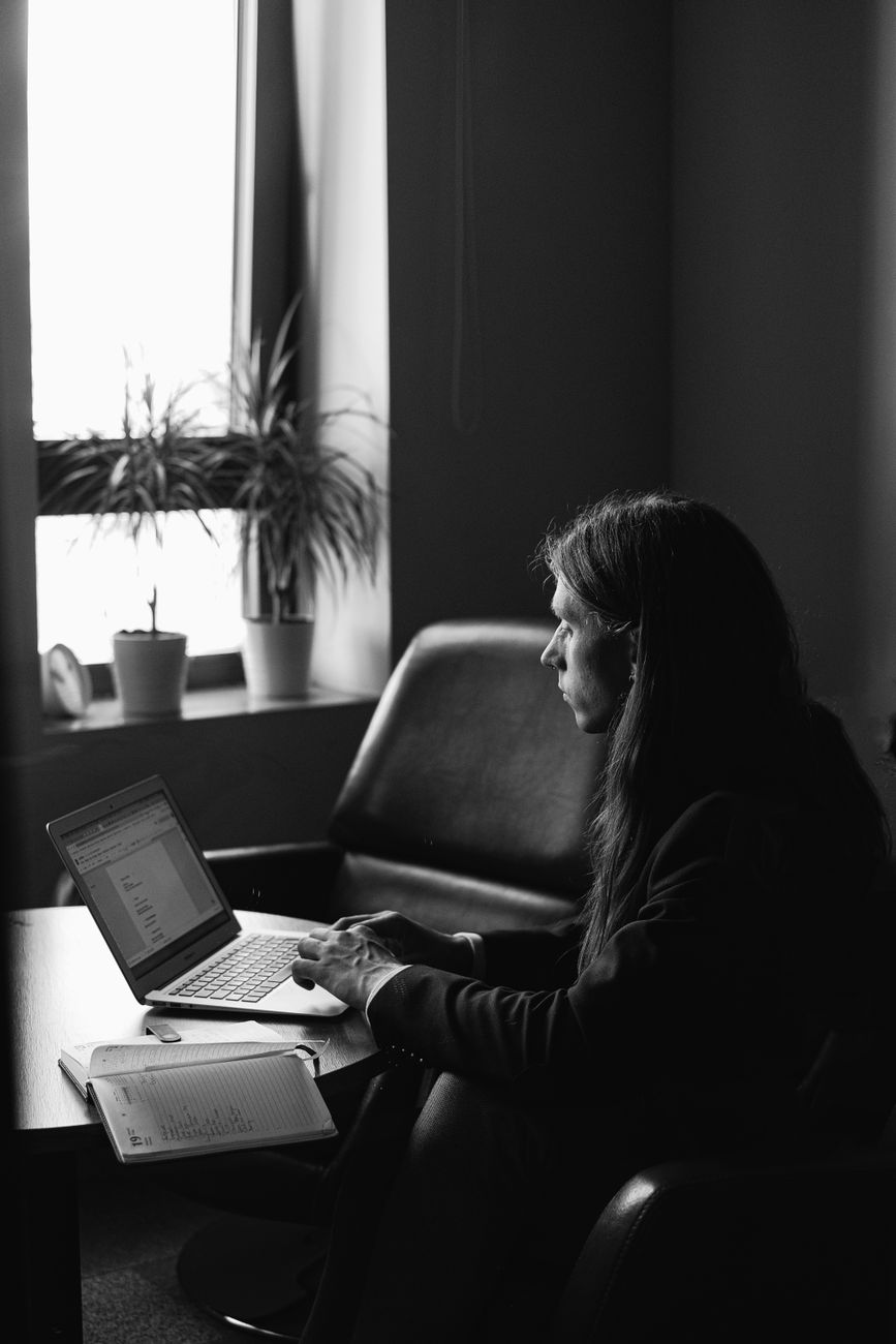 Black and white of focused freelancer sitting at table near window and using laptop while working on project in workspace