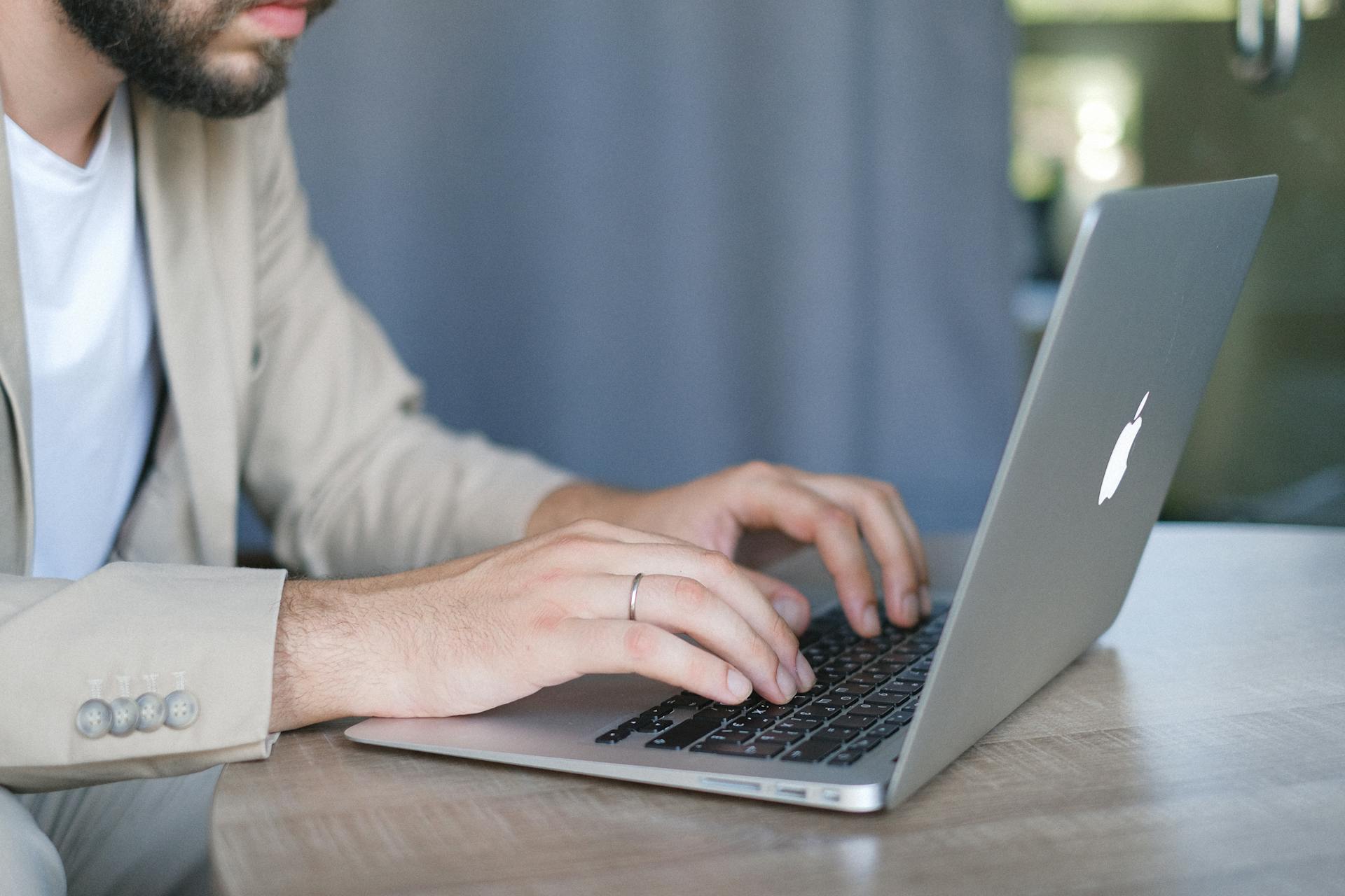 A young man in a beige suit typing on a laptop in a bright, modern office space.