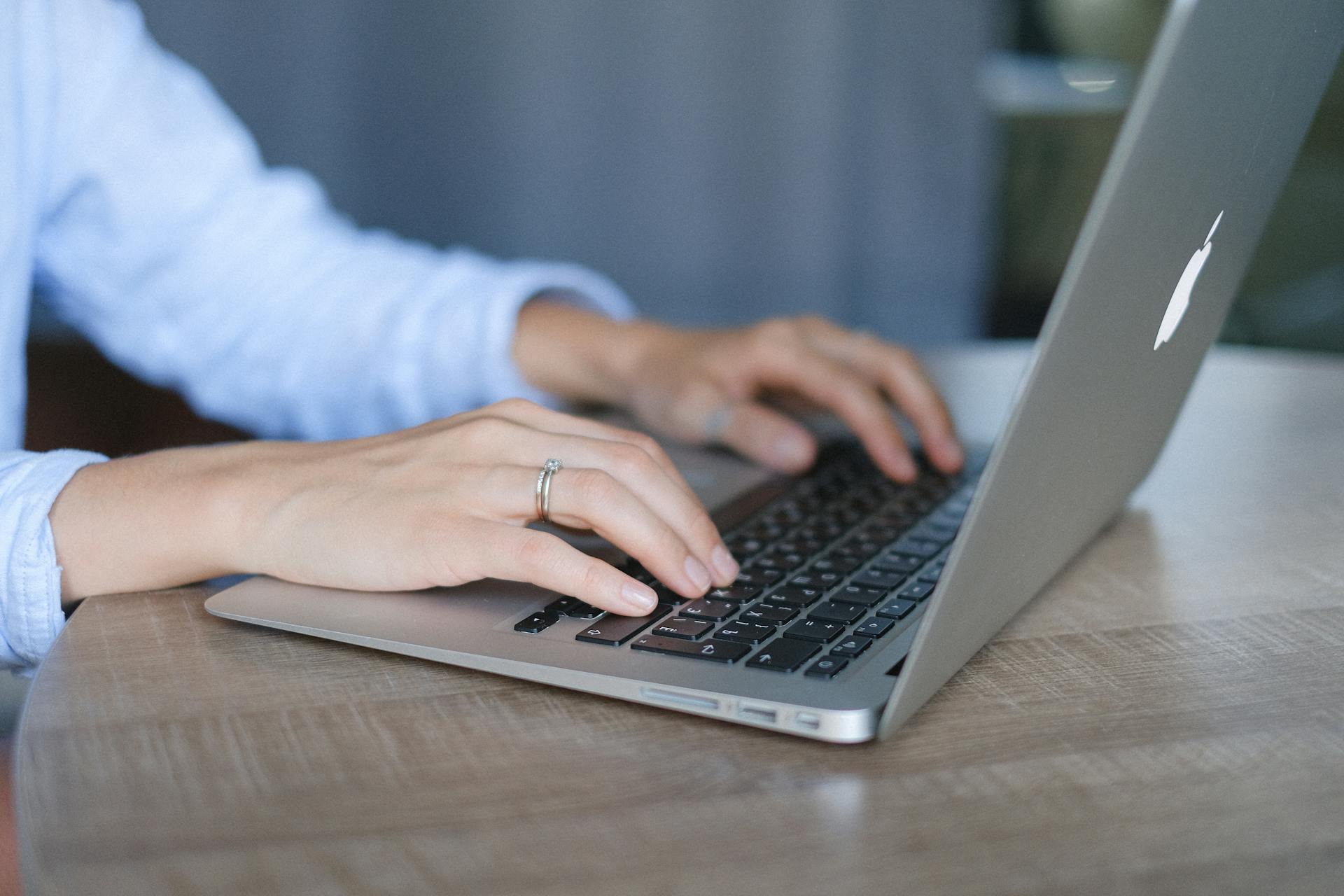 Crop faceless female entrepreneur wearing casual clothes sitting at wooden desk and browsing portable netbook in daylight