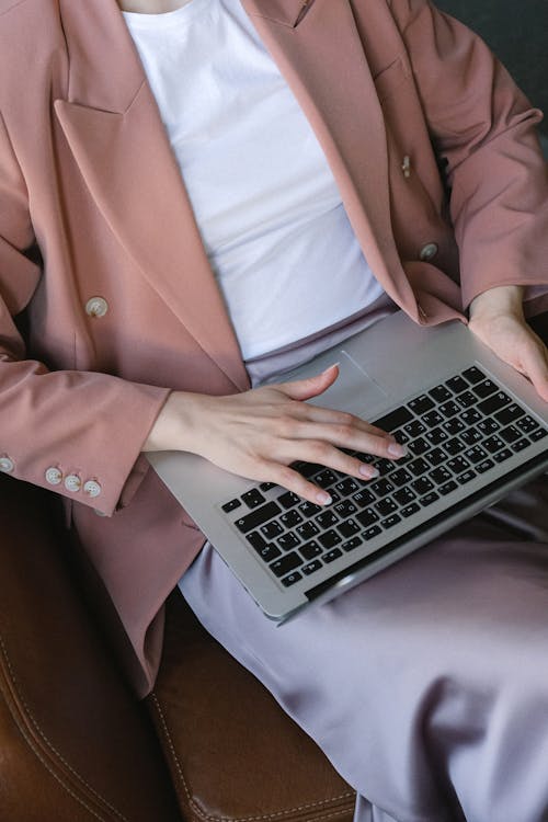 Free From above of crop anonymous female employee wearing formal clothes sitting in comfortable armchair with laptop on knees and working remotely Stock Photo