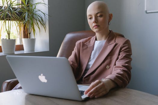 Bald businesswoman in a suit working on a laptop in a bright office setting.