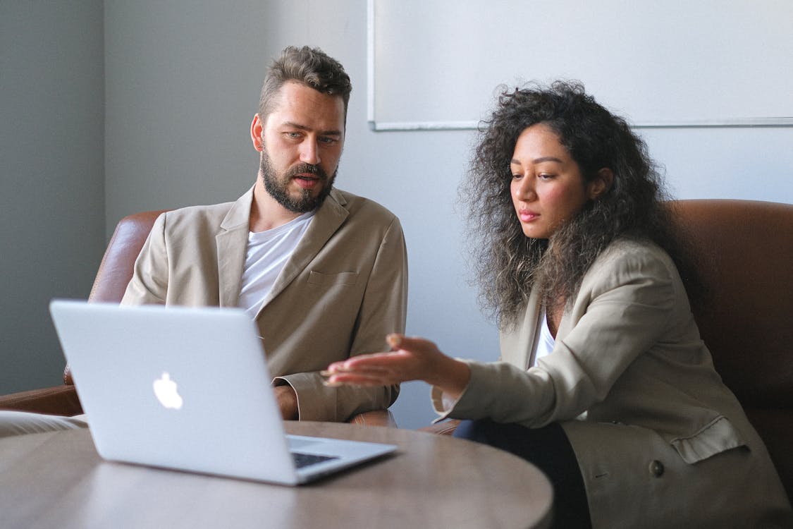 Two people using a laptop while discussing a new project. representing the importance of technical documentation writers.