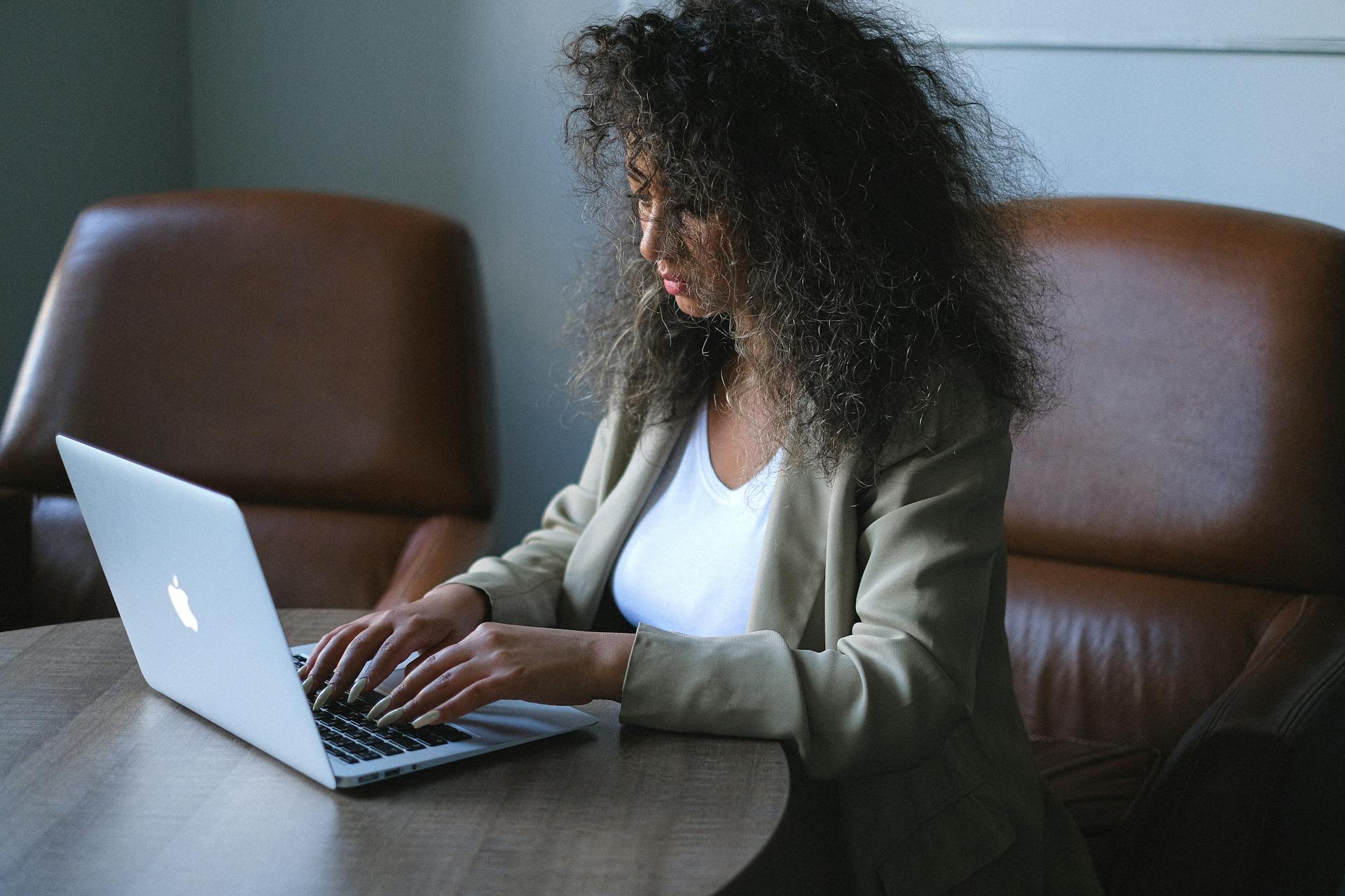 Side view of young ethnic female in stylish outfit browsing laptop while sitting at table and working on project in office