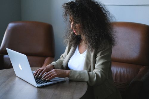 Free Side view of young ethnic female in stylish outfit browsing laptop while sitting at table and working on project in office Stock Photo