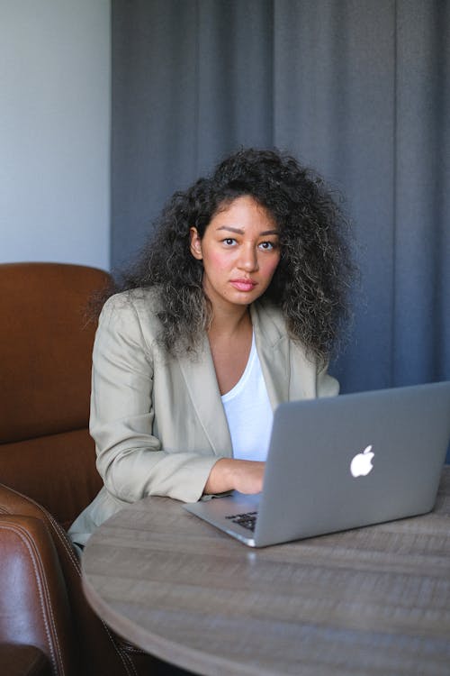 Concentrated woman with curly hair wearing formal clothes sitting at table in office and browsing netbook