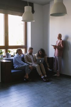 Full body of focused colleagues discussing business project while using laptop and tablet in modern workplace