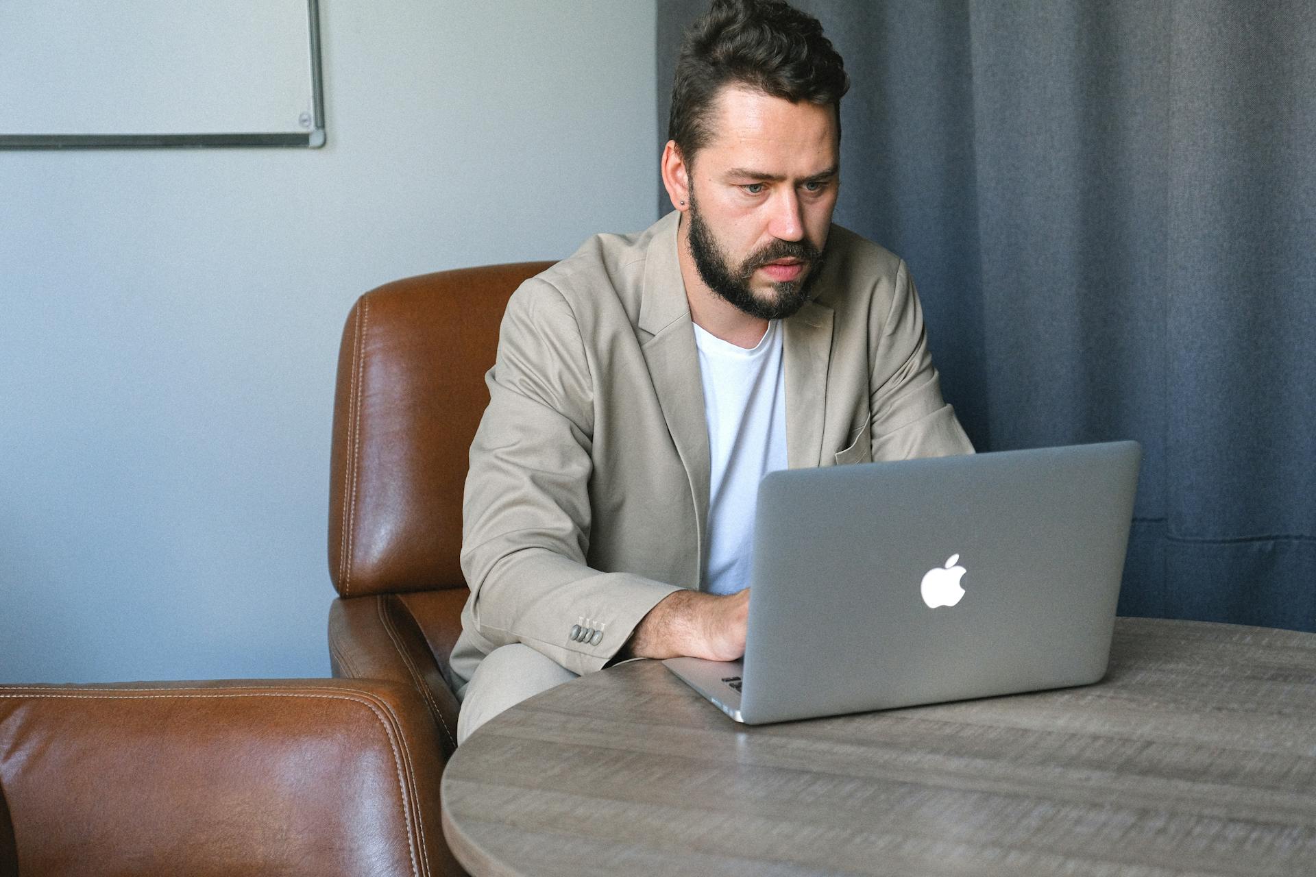 Concentrated bearded male entrepreneur wearing formal suit browsing netbook while working on startup