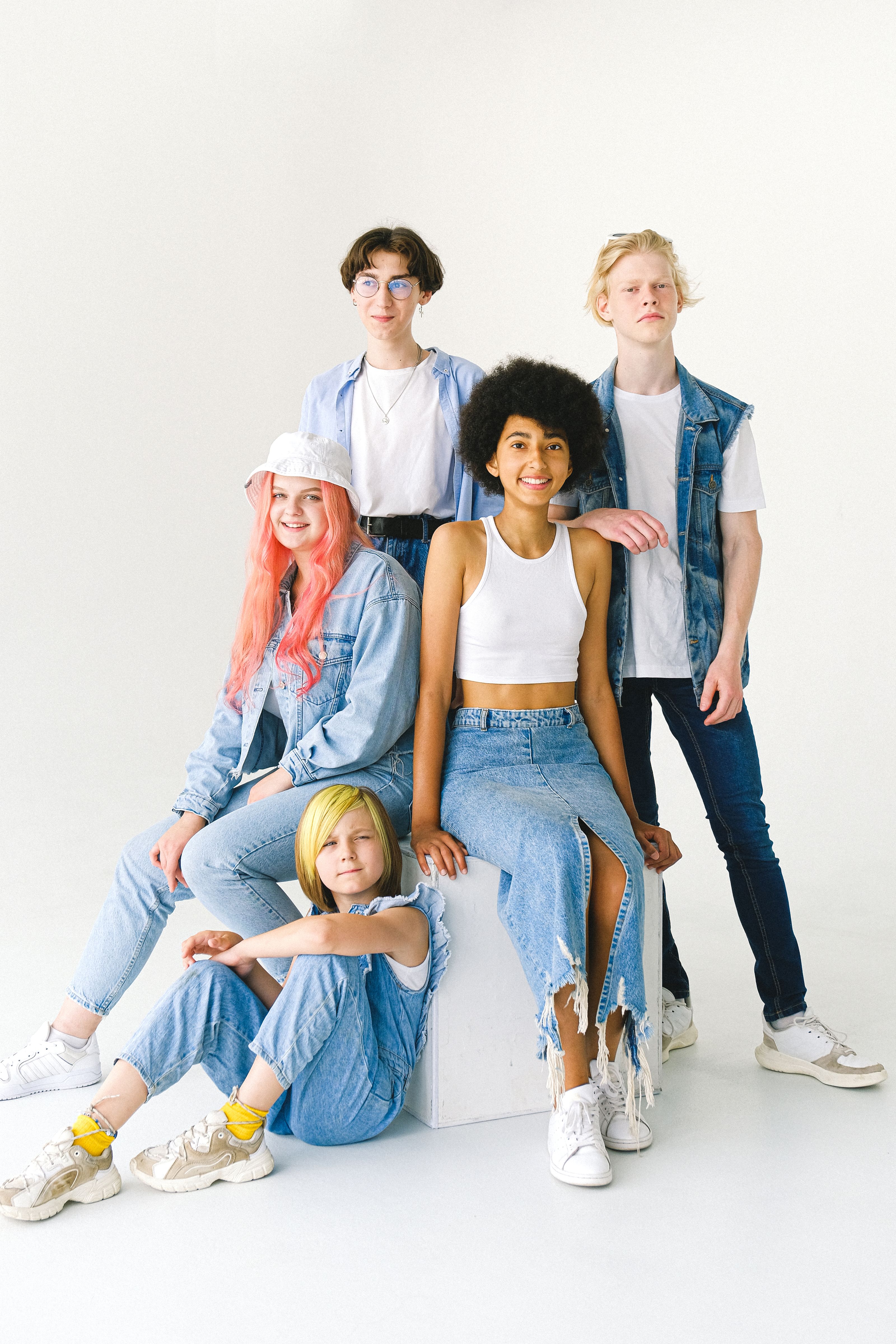 Grupo de adolescentes estilosos em roupas de denim posando com sorrisos brilhantes em um fundo branco.