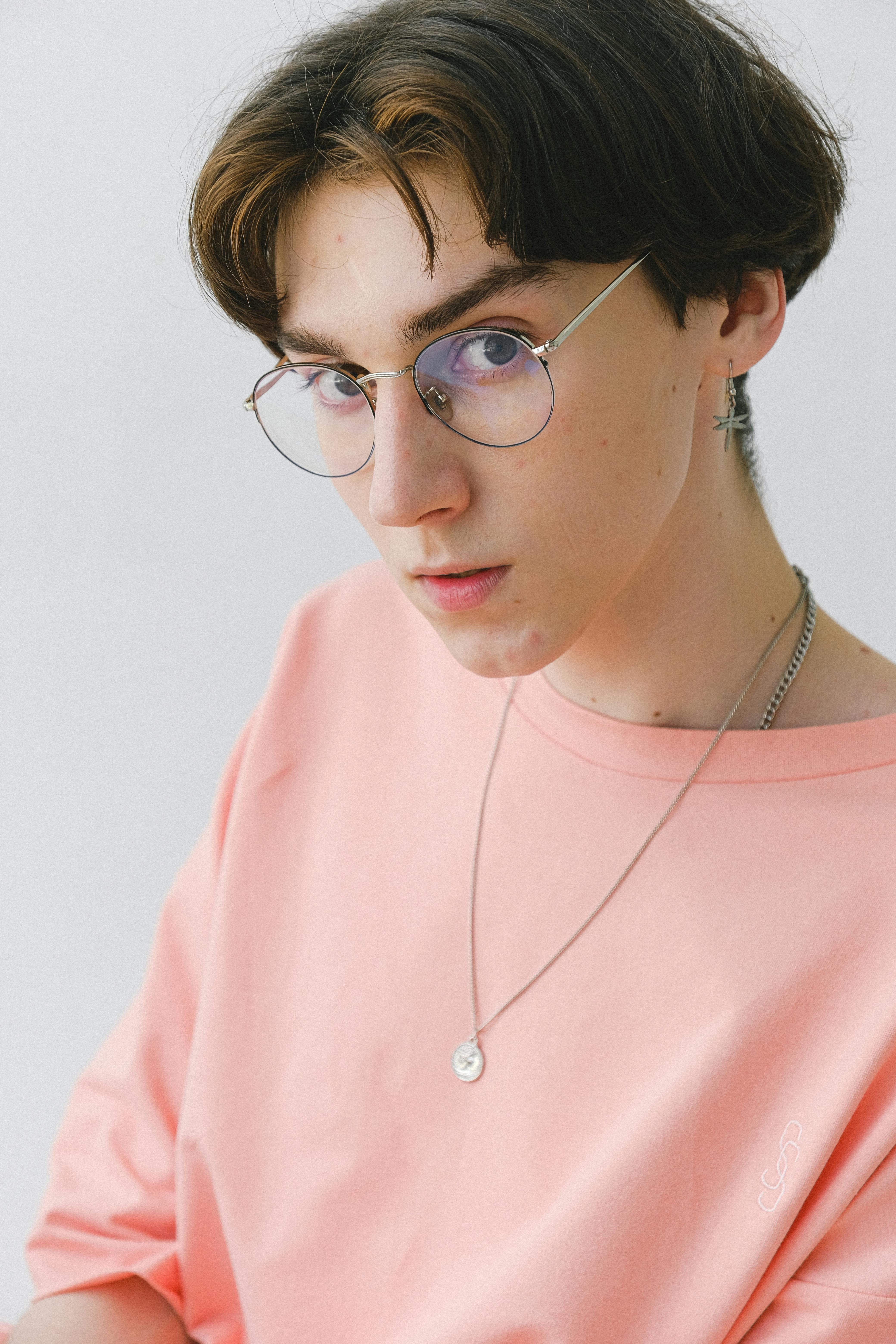 confident stylish teen man in eyeglasses and necklace in studio