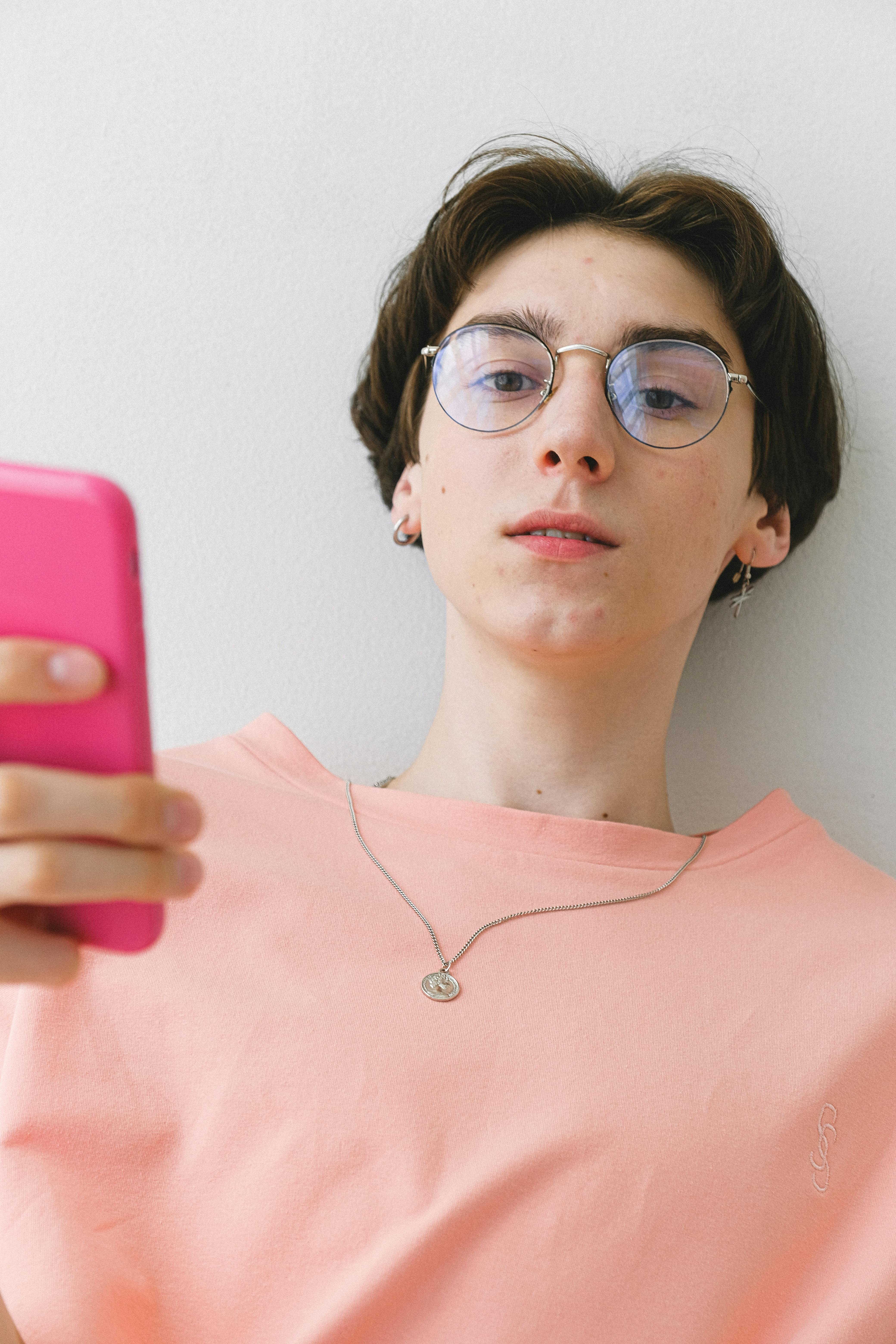 young man in stylish eyewear and piercing browsing smartphone
