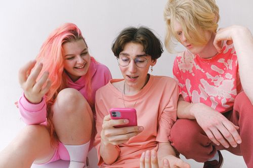 Free Informal teenagers in pink outfits sitting together and browsing internet in smartphone while watching funny videos Stock Photo