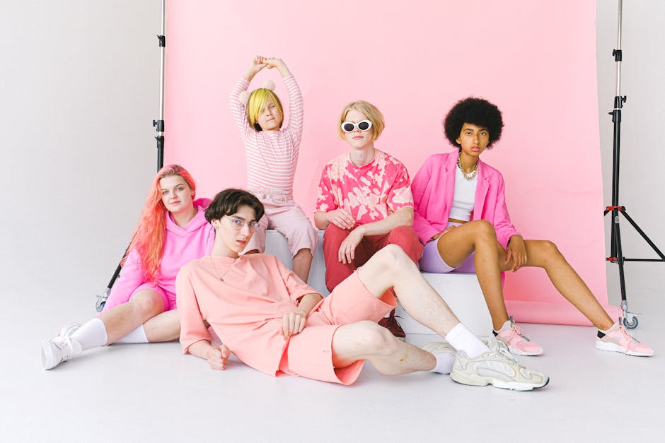 Full length calm informal diverse teenage friends in pink outfits sitting near pink backdrop and looking at camera