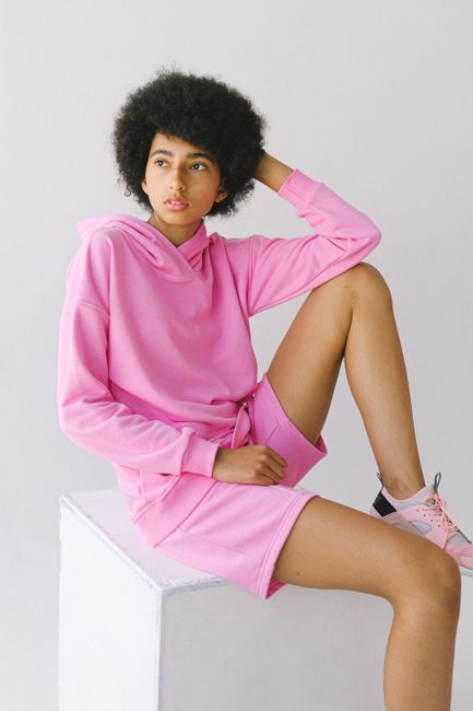 Contemplative young African American female in pink outfit with afro hairstyle looking away touching head on white background