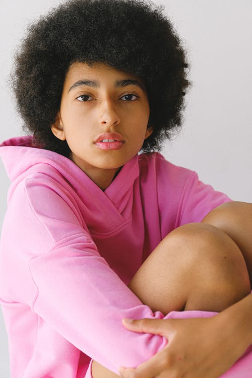 Free Calm young African American female in pink clothes with afro haircut with arms on legs looking at camera Stock Photo