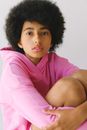 Calm young African American female in pink clothes with afro haircut with arms on legs looking at camera