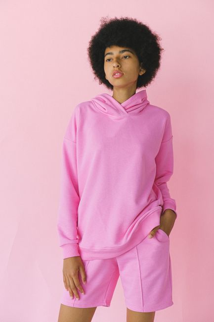 Fashionable adult woman in a vibrant pink outfit posing against a soft background.