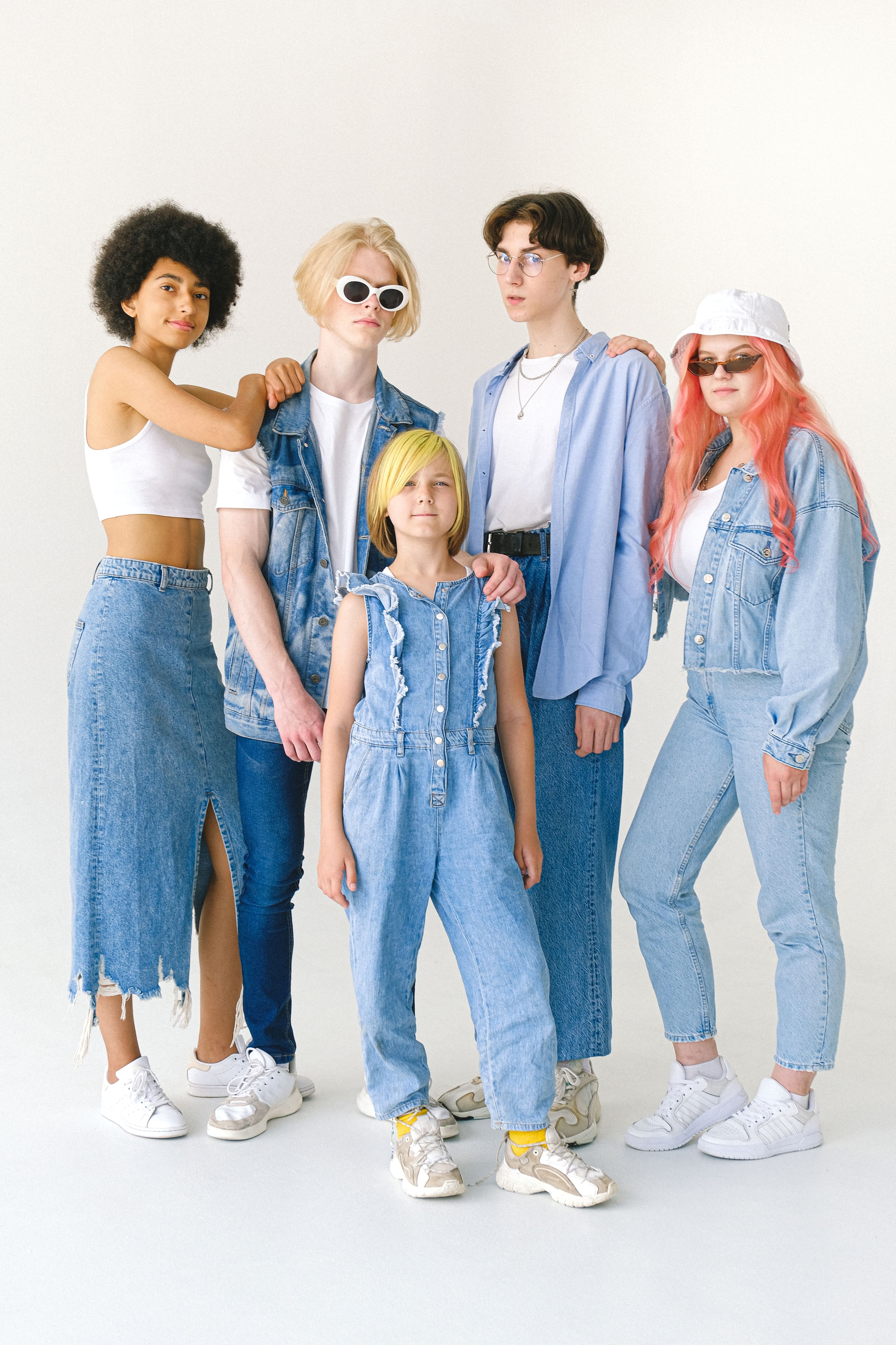 Um grupo de adolescentes fashion posando em roupas de jeans contra um fundo branco, destacando diversidade e estilo.