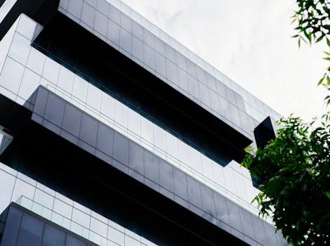 低角度视角下的现代摩天大楼，其几何玻璃立面映照着多云的天空