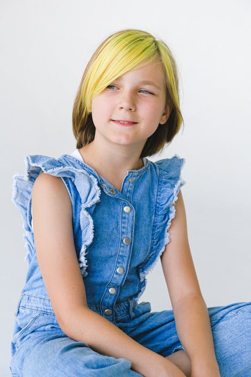 Cheerful girl with dyed hair in sleeveless denim overall on white background looking away