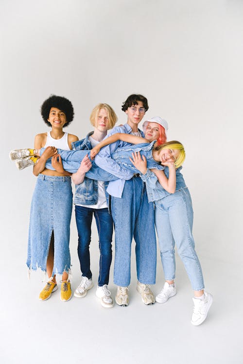 Full length of multiracial friends in casual clothes standing in studio while holding child on hands on white background while looking at camera