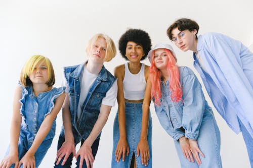 From below of group of cheerful teenager friends wearing denim clothes standing against white background and looking at camera