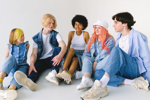 Group of cheerful diverse teenager friends talking to each other while sitting together on floor against white background
