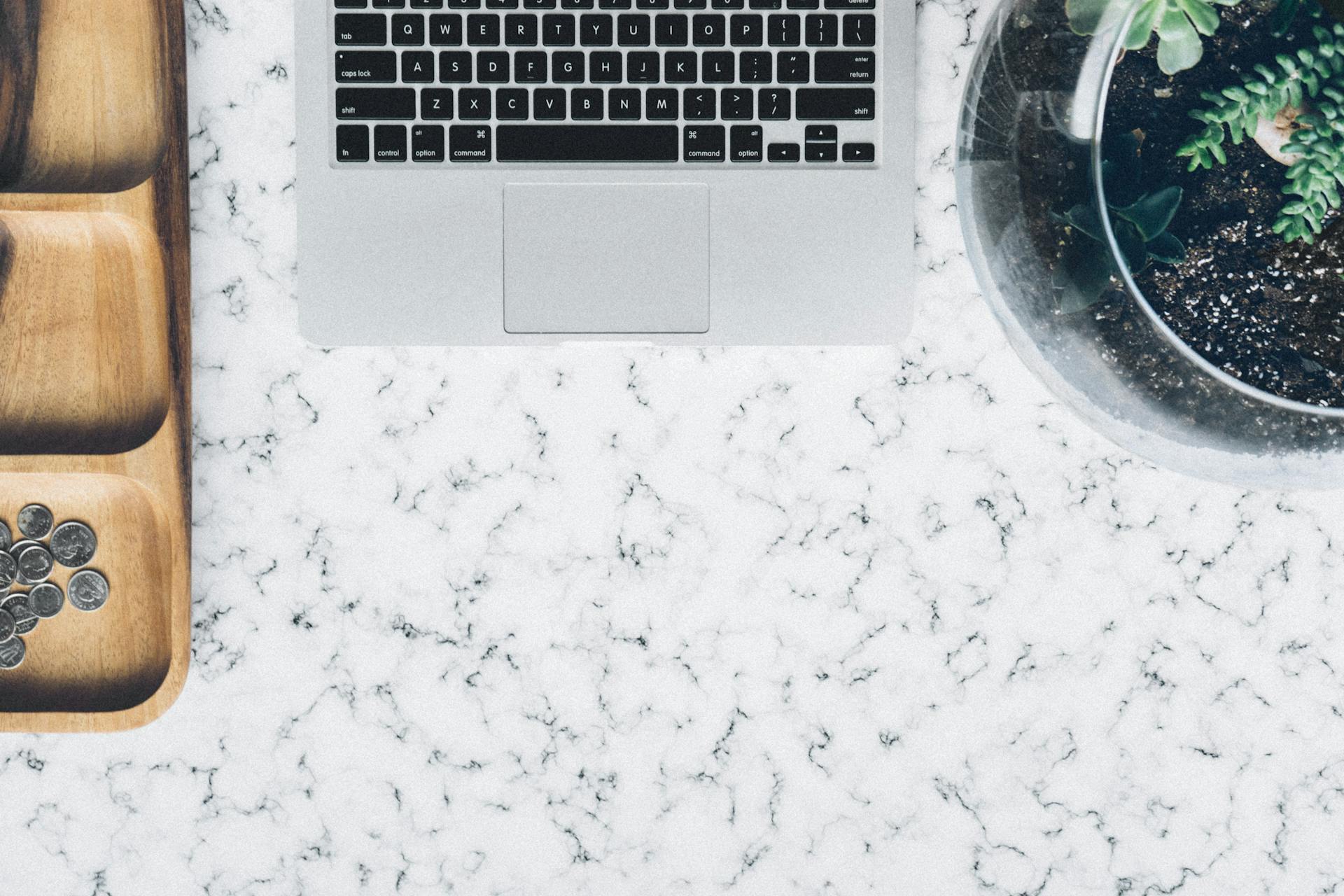 Top view of a contemporary workspace featuring a laptop, plant, and coins on a marble surface.