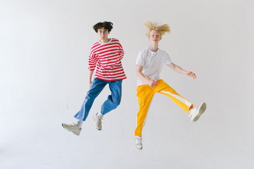 Full body cheerful teenager friends in colorful wear jumping high on white background and looking at camera