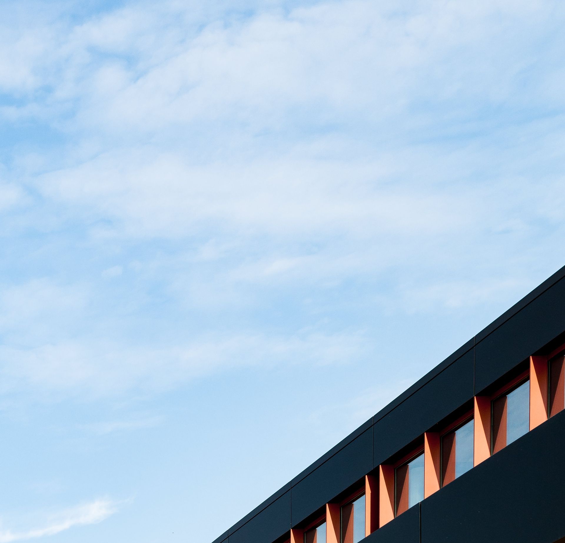 Low angle view of a modern flat building with glass windows against a clear blue sky.