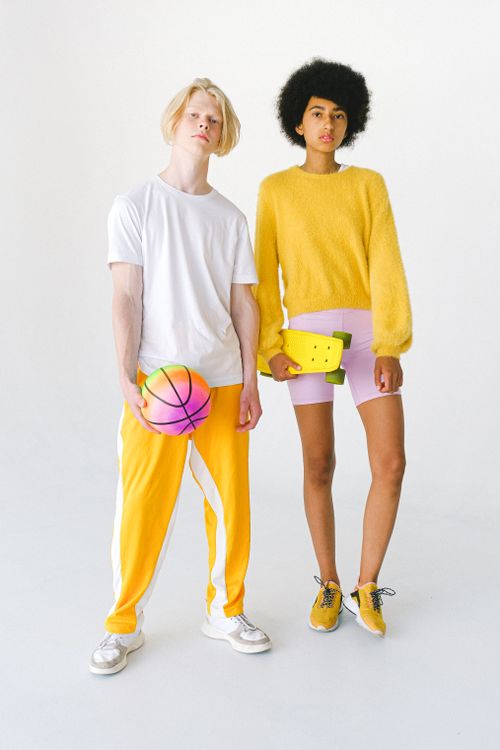 Free Full body informal multiethnic couple in bright colorful wear with multicolored ball for basketball and yellow penny board against white background looking at camera Stock Photo