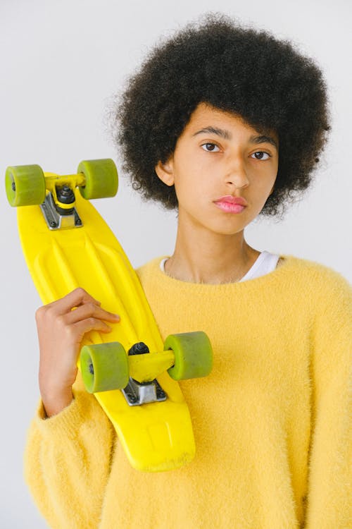 Calm informal teenage African American female skater with yellow penny board on white background looking at camera