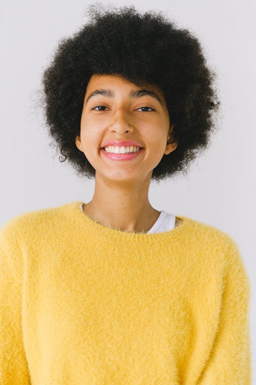 Happy young African American female in vivid yellow sweater against white background looking at camera smiling