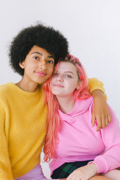 Free Diverse cheerful teenage girls looking at camera in bright yellow sweater and pink hoodie on white background Stock Photo