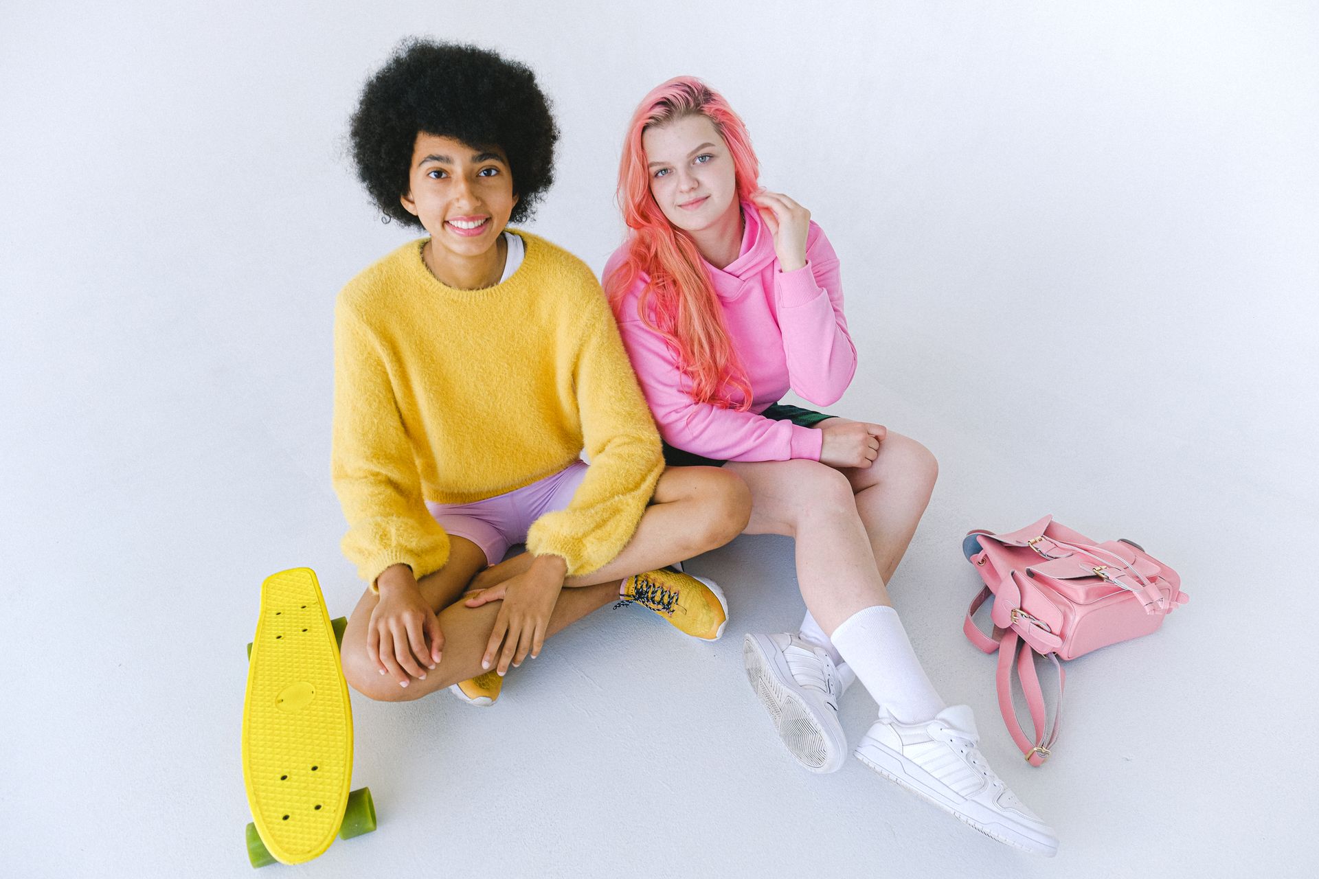 Delighted multiethnic teenage girls with skateboard and stylish backpack