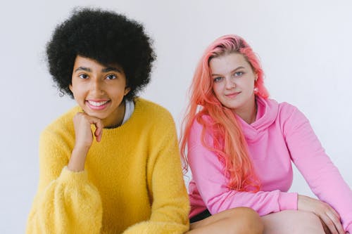 Happy diverse teenagers in bright outfit smiling and looking at camera on white background of studio