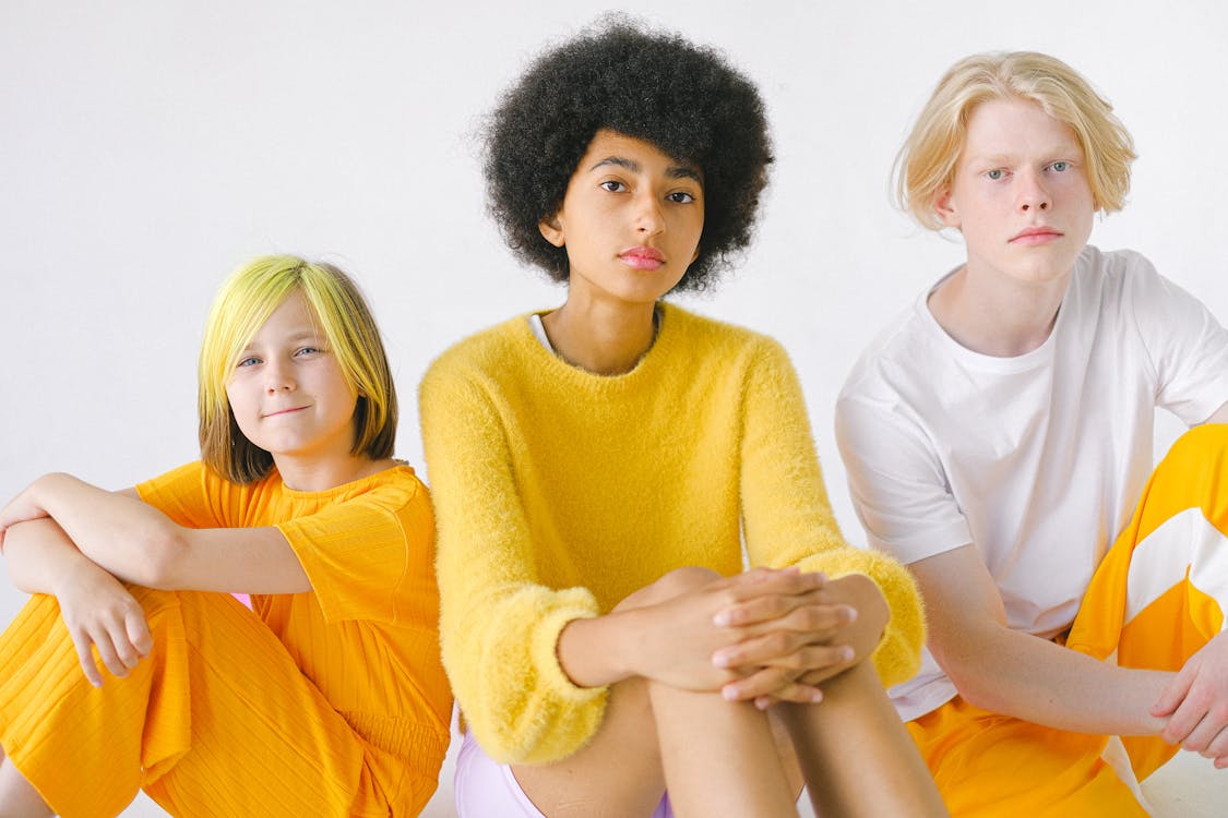 Diverse teenagers in bright yellow outfits with dyed hair and Afro hairstyle looking at camera on white background