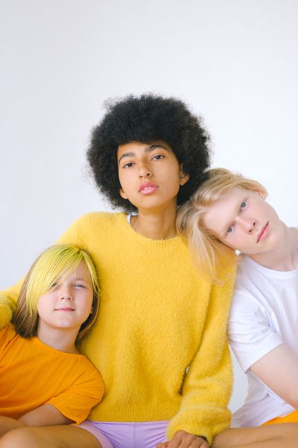 Three diverse teenagers embracing in a bright yellow and white background.