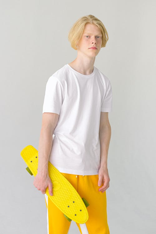 Free Slender teenager in bright casual outfit with colorful yellow skateboard on white background os studio Stock Photo