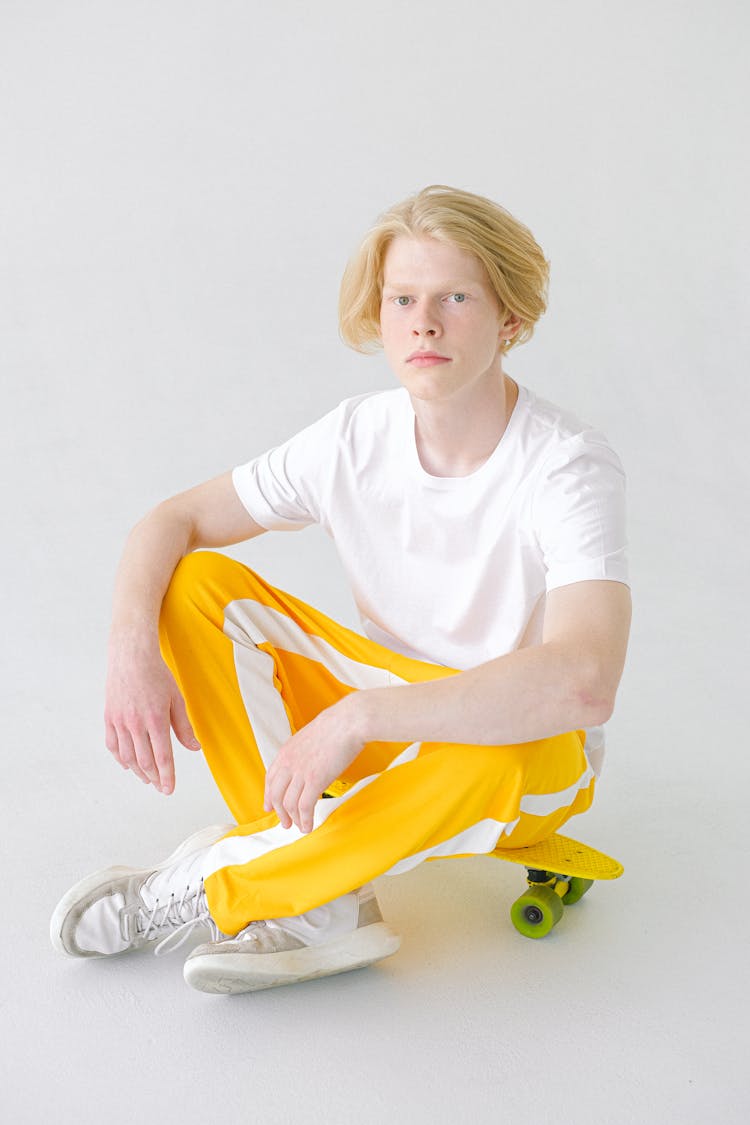 Teenager In Bright Yellow Trousers Resting On Skateboard