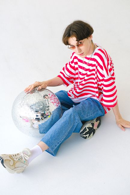 From above of teenage boy in eyeglasses and red and white striped T shirt with disco ball looking at camera